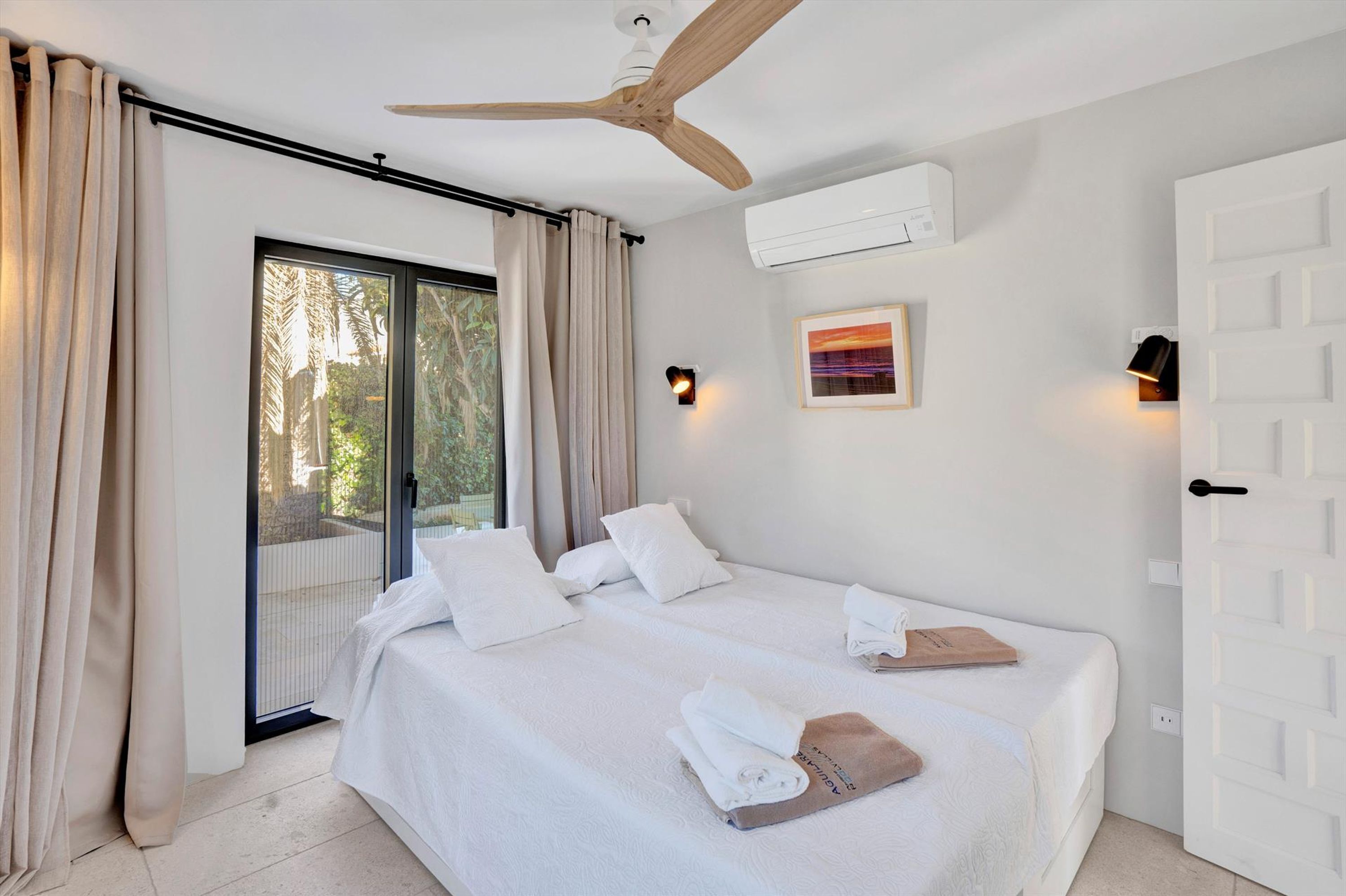 Une chambre d’hôtel avec un lit, des rideaux, un ventilateur de plafond, un appareil de climatisation et une porte.