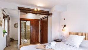 Una camera d'albergo con un letto, una porta in legno, una doccia e un comodino con una lampada.
