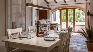 Zona pranzo con tavolo apparecchiato per due, una bottiglia d'acqua e una ciotola di frutta. Si vede una finestra con vista sul verde.