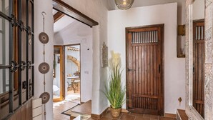 Un corridoio con una porta in legno, un elemento decorativo appeso e una pianta in vaso.