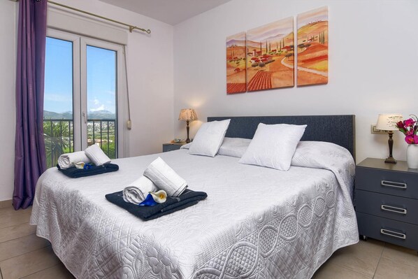 A hotel room with a large bed, a nightstand with a lamp, a view of the outdoors through a balcony, and artwork on the wall. - El Elefante in J vea (Javea)