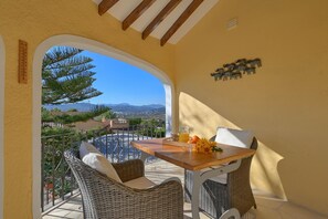 Relax on the balcony with a view of the surrounding landscape, featuring a wicker sofa, wooden table, and decorative metal wall piece.