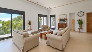 A spacious living room with a sofa set, a coffee table, and a view of greenery through large windows. - Casa Renata 8 pax in Javea (Javea)