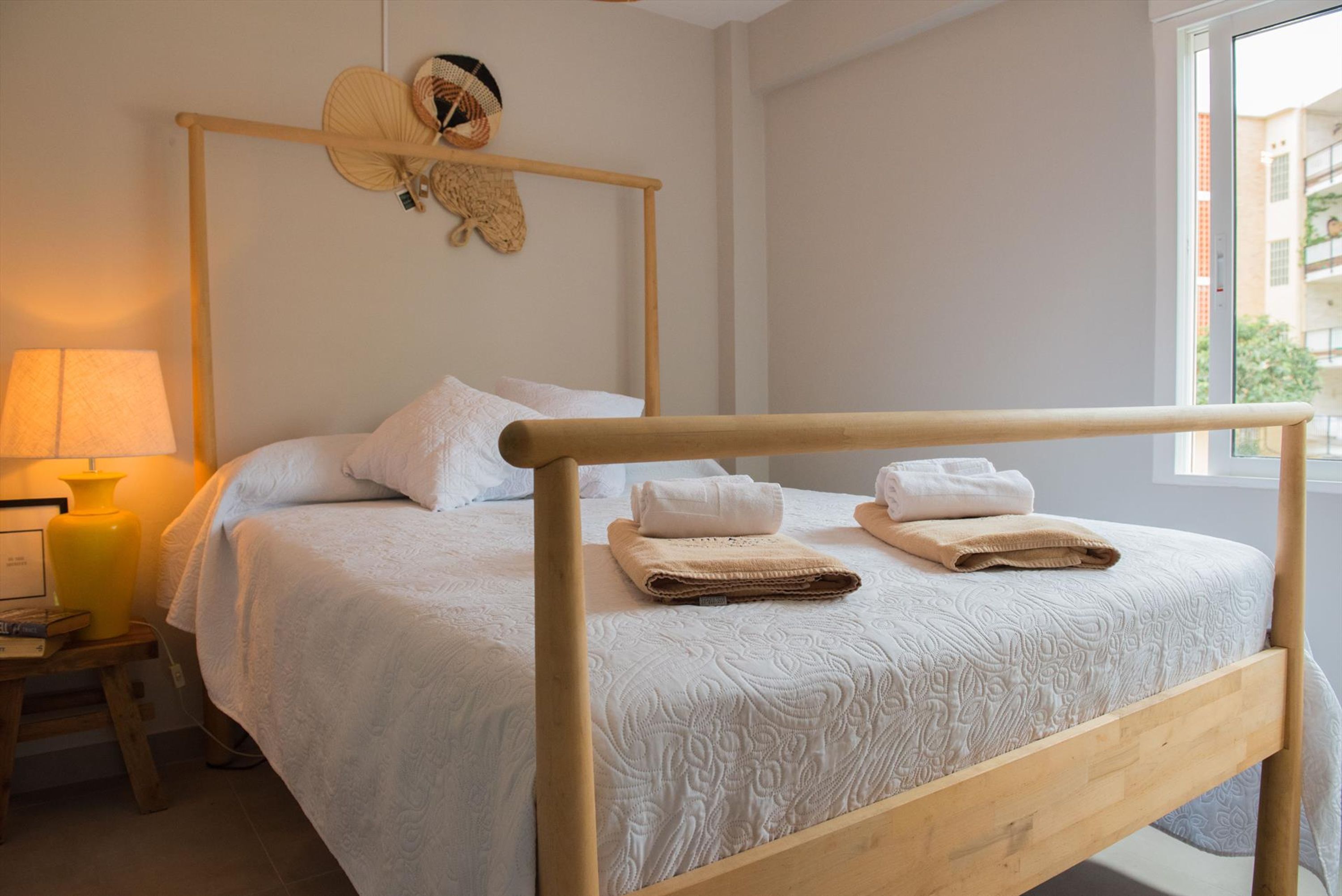 A neatly made bed with a wooden headboard, a bedside lamp, and a wall-mounted hat rack.
