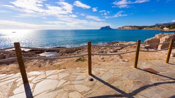 A stone pathway leading to a beach with a clear view of the sea and a distant island.