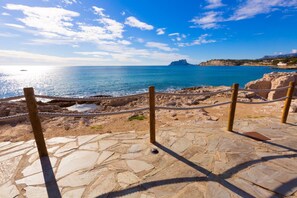 Un sentiero in pietra conduce a una spiaggia con vista limpida sul mare e un'isola in lontananza.