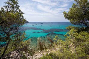 Paesaggio costiero con acque turchesi limpide, imbarcazioni e terreno roccioso.