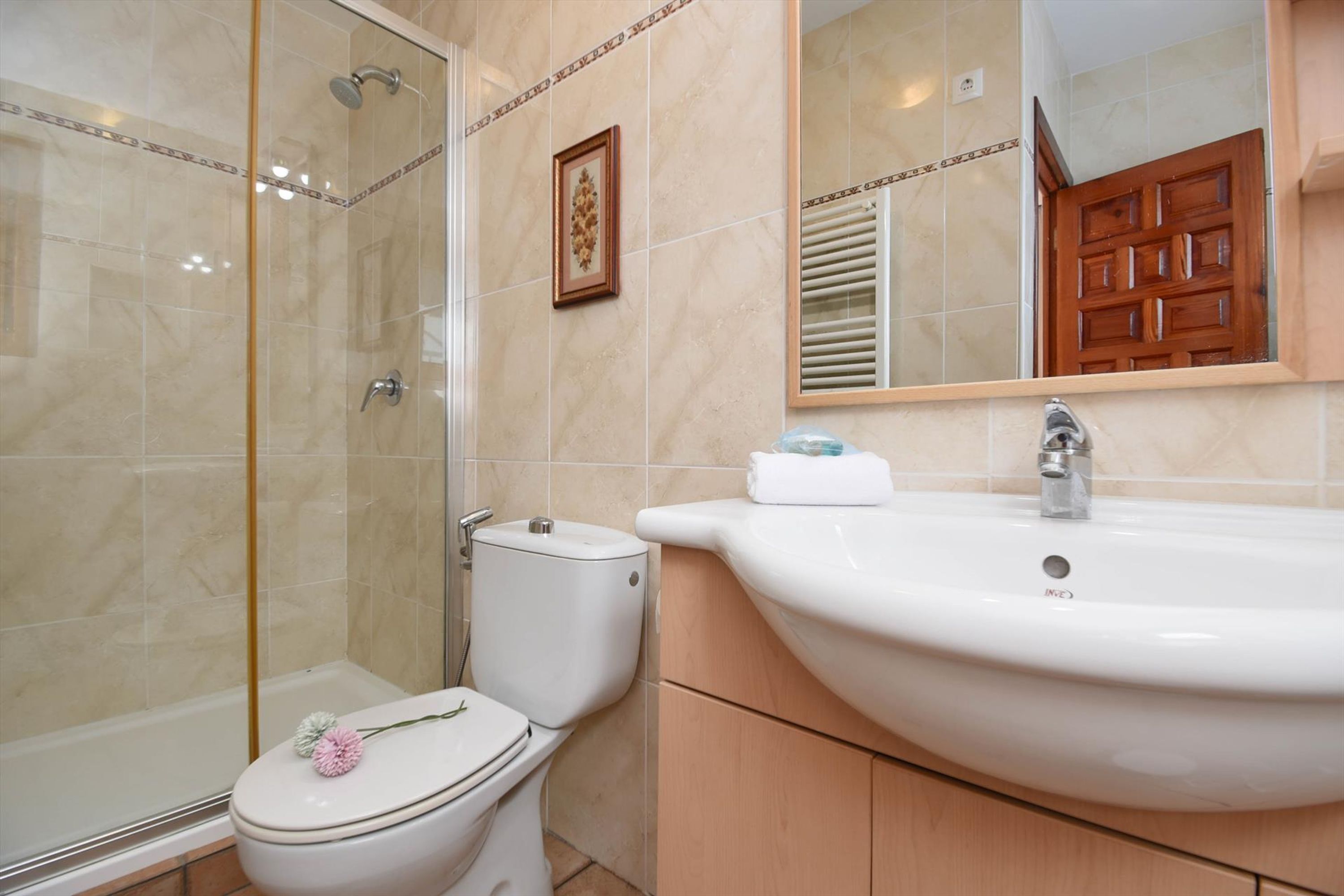 Ein Badezimmer mit einer gläsernen Duschkabine, einer Toilette und einem Waschbecken mit Spiegel darüber.