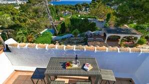 Eine Terrasse mit gedecktem Tisch für zwei Personen, mit Blick auf eine reizvolle Landschaft, inklusive Pool und üppiger Bepflanzung.