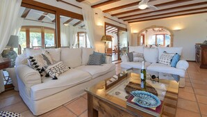 Ein geräumiges Wohnzimmer mit zwei weißen Sofas, einem Glastisch und Holzbalken an der Decke.