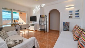Een moderne hotelkamer met een balkon, een flatscreen televisie, een boekenkast en een zithoek met een tafel en stoelen.