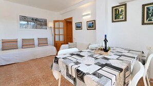 Een kamer met een bed, een eettafel met stoelen, een lamp en wanddecoraties in lijsten.
