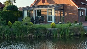 Ein Haus mit Backsteinfassade, einer überdachten Terrasse und einem Teich im Vordergrund.