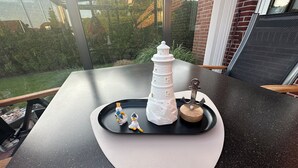 Ein Tisch mit einer Ablage, auf der ein weißes Leuchtturmmodell, ein hölzerner Anker und zwei Entenfiguren platziert sind.