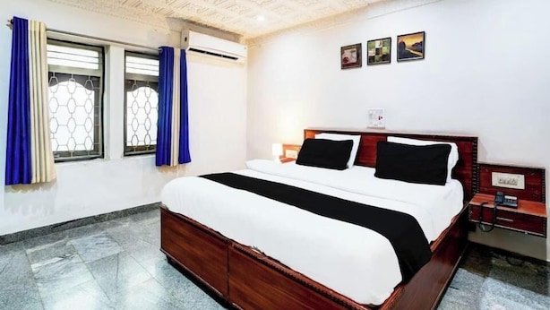 Ein Hotelzimmer mit einem großen Bett, einem Holzkopfteil, einem Nachttisch und einem Fenster mit Vorhängen.