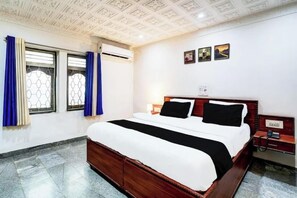Une chambre d’hôtel avec un grand lit, une tête de lit en bois, une table de chevet et une fenêtre avec des rideaux.