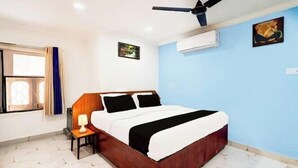 Ein Schlafzimmer mit einem Bett, einem Deckenventilator, einer Klimaanlage, einem Fenster mit Vorhängen und einem kleinen Tisch mit einer Lampe.