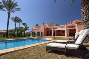 A poolside area with lounge chairs, a swimming pool, and a building with a red facade and columns. - Mozamb in J vea With 4 Bedrooms and 3 Bathrooms (Javea)