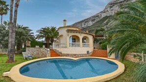 Un espace aménagé au bord d’une piscine, avec une piscine, un petit bâtiment doté d’un balcon et un paysage montagneux en arrière-plan.
