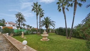 Un jardin bien entretenu, agrémenté d’un chemin de pierres, de palmiers et d’une fontaine décorative.