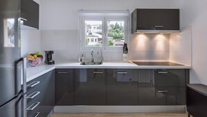 Een moderne keuken met donkere kastjes, een wit aanrecht, een roestvrijstalen koelkast en een raam met uitzicht op gebouwen en bomen.