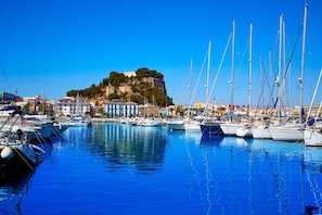A marina with boats docked, a prominent hill with buildings, and clear blue skies.