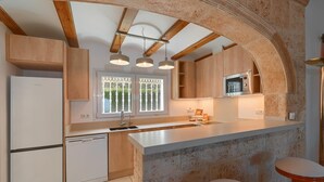 A modern kitchen with wooden cabinets, a built-in microwave, and a large island with stools. - Serena Vista in J vea (Denia)