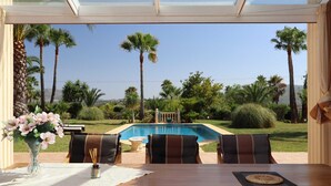 A patio with a table and chairs overlooking a swimming pool, surrounded by palm trees and a clear sky. - Mozamb 6 pax in J vea (Javea)