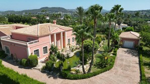 A pink villa with a tiled roof, a swimming pool, and a well-maintained garden with palm trees. - Mozamb 6 pax in J vea (Javea)