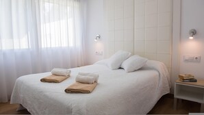 A neatly made bed with white linens and two beige towels, a bedside table with a book, and a wall-mounted light fixture. - Marina B5 in El Tosalet (Denia)