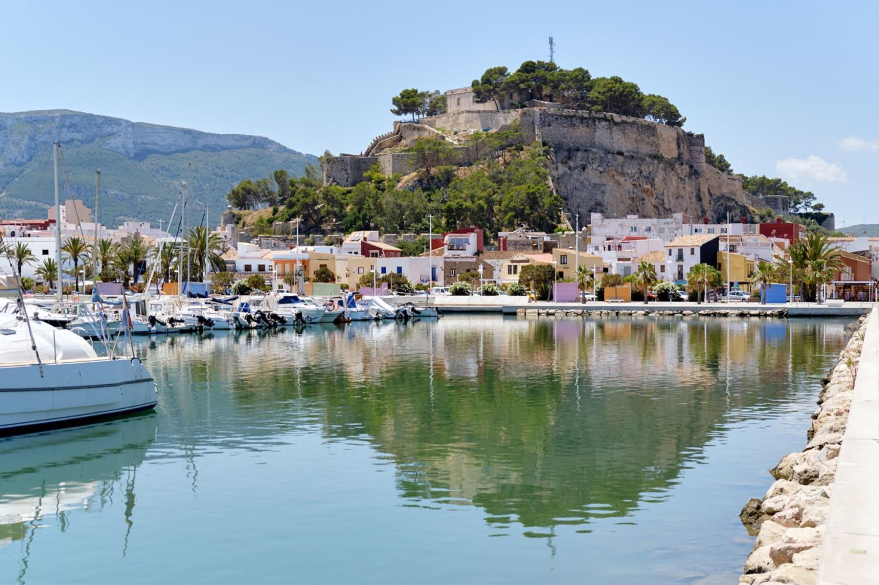 A marina with boats docked, a coastal town with buildings, and a castle on a hill.