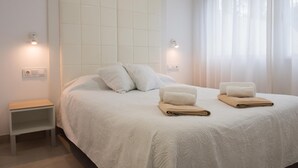 A neatly made bed with pillows and folded towels, a bedside table, and wall-mounted lights. - Marina B3 in J vea With 3 Bedrooms and 2 Bathrooms (Denia)