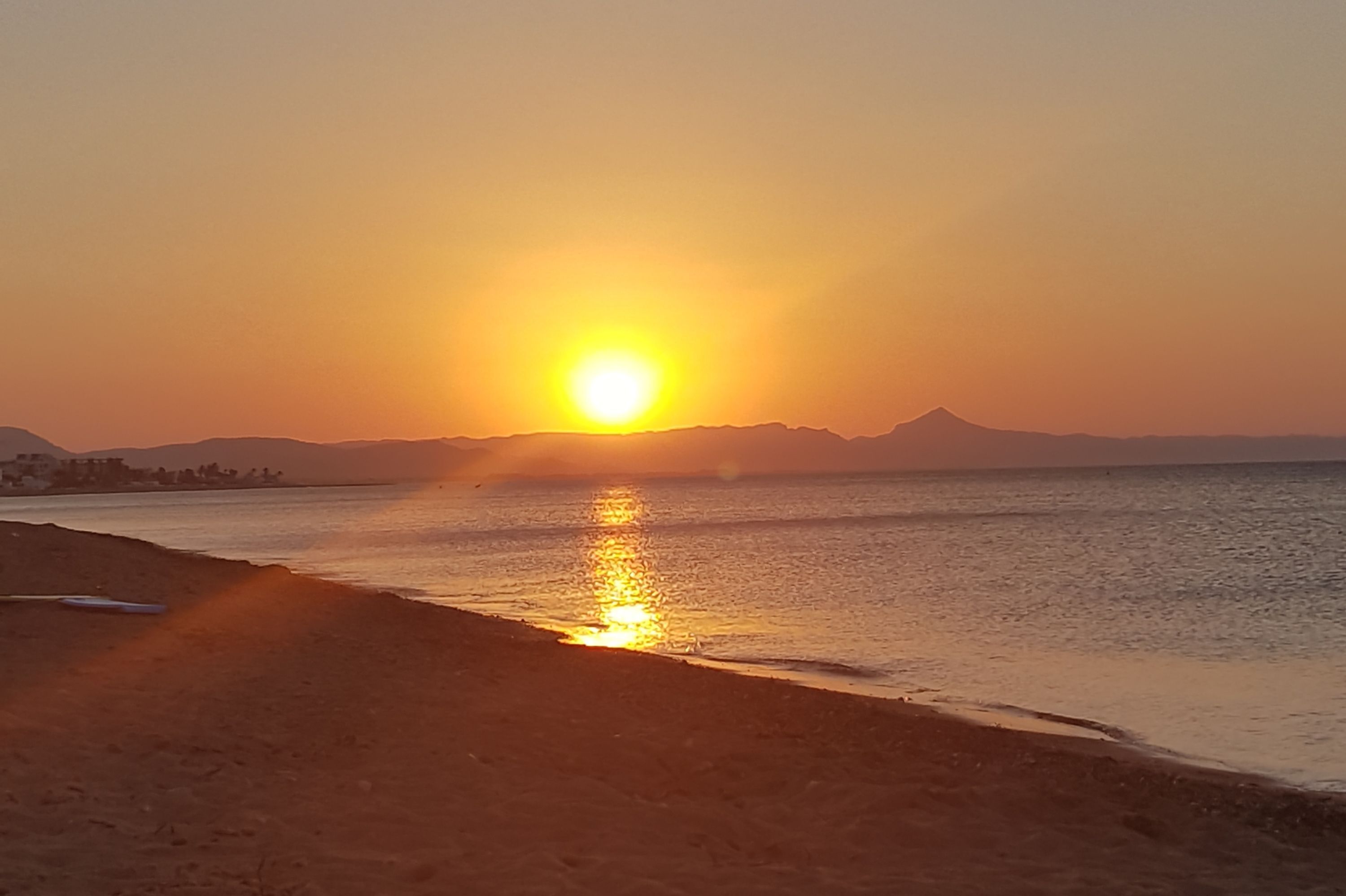 A sunset over a beach with a mountain in the background.