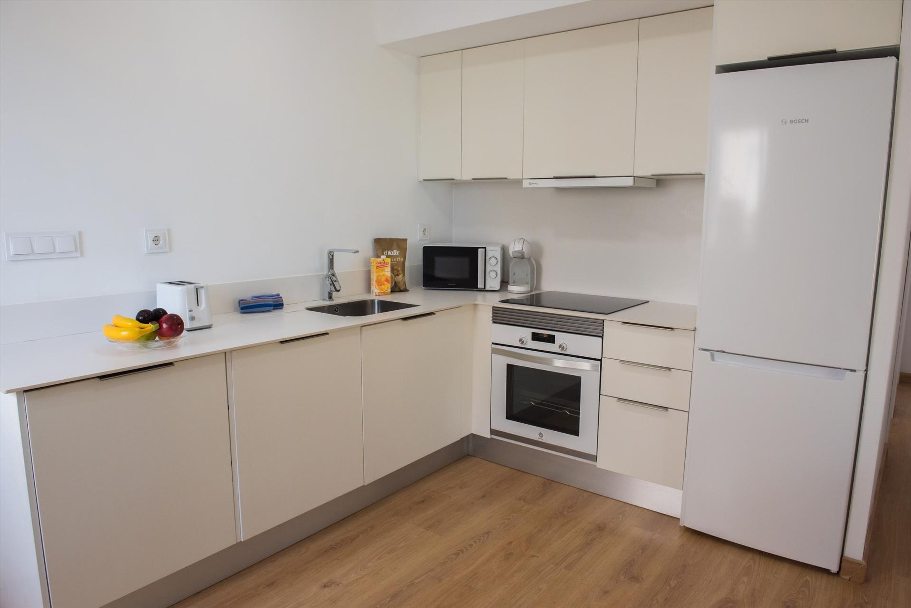 A modern kitchen with white cabinets, a microwave, a coffee maker, and a Bosch refrigerator.