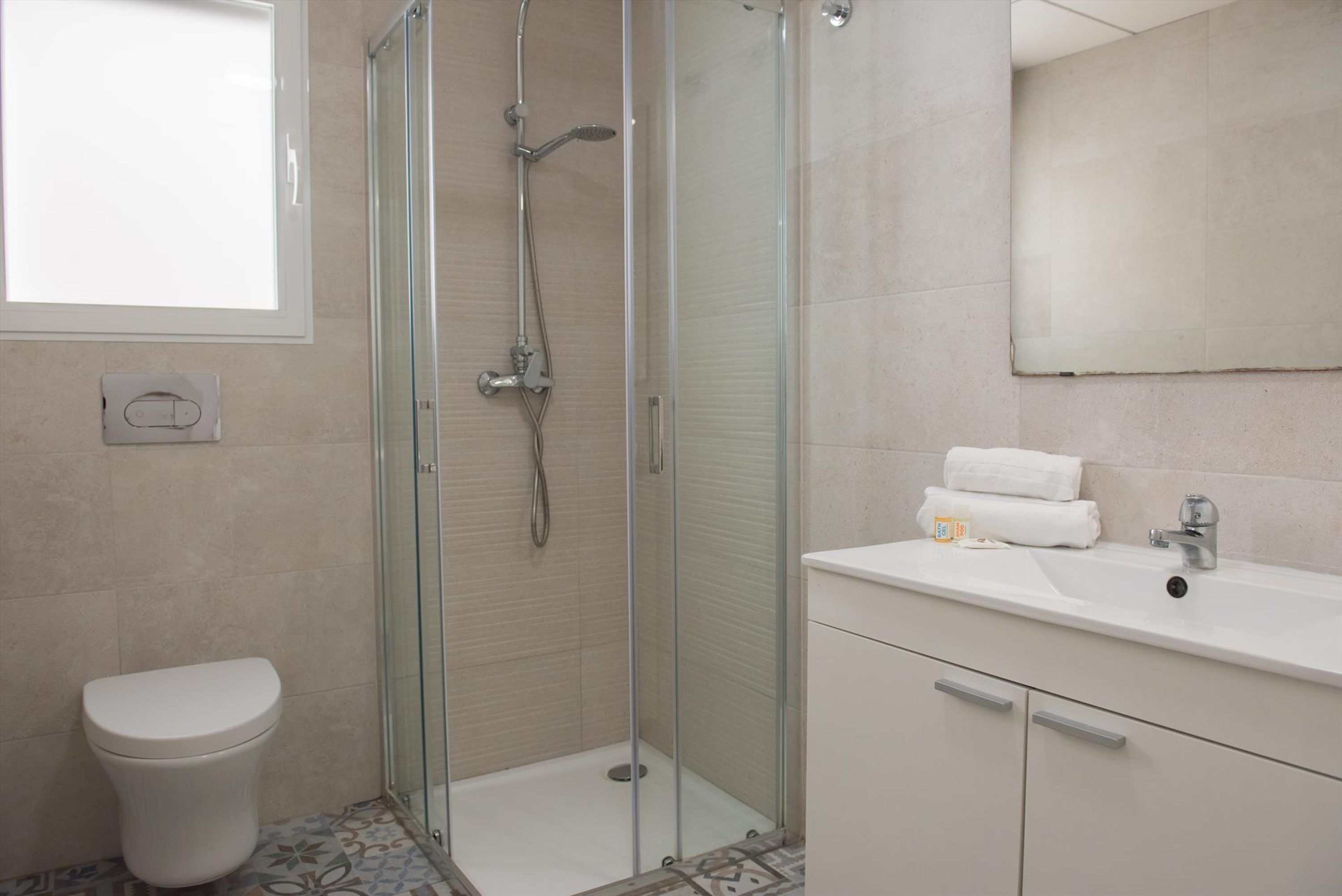 Une salle de bain moderne avec une douche à parois de verre, des toilettes blanches et un lavabo surmonté d’un miroir.