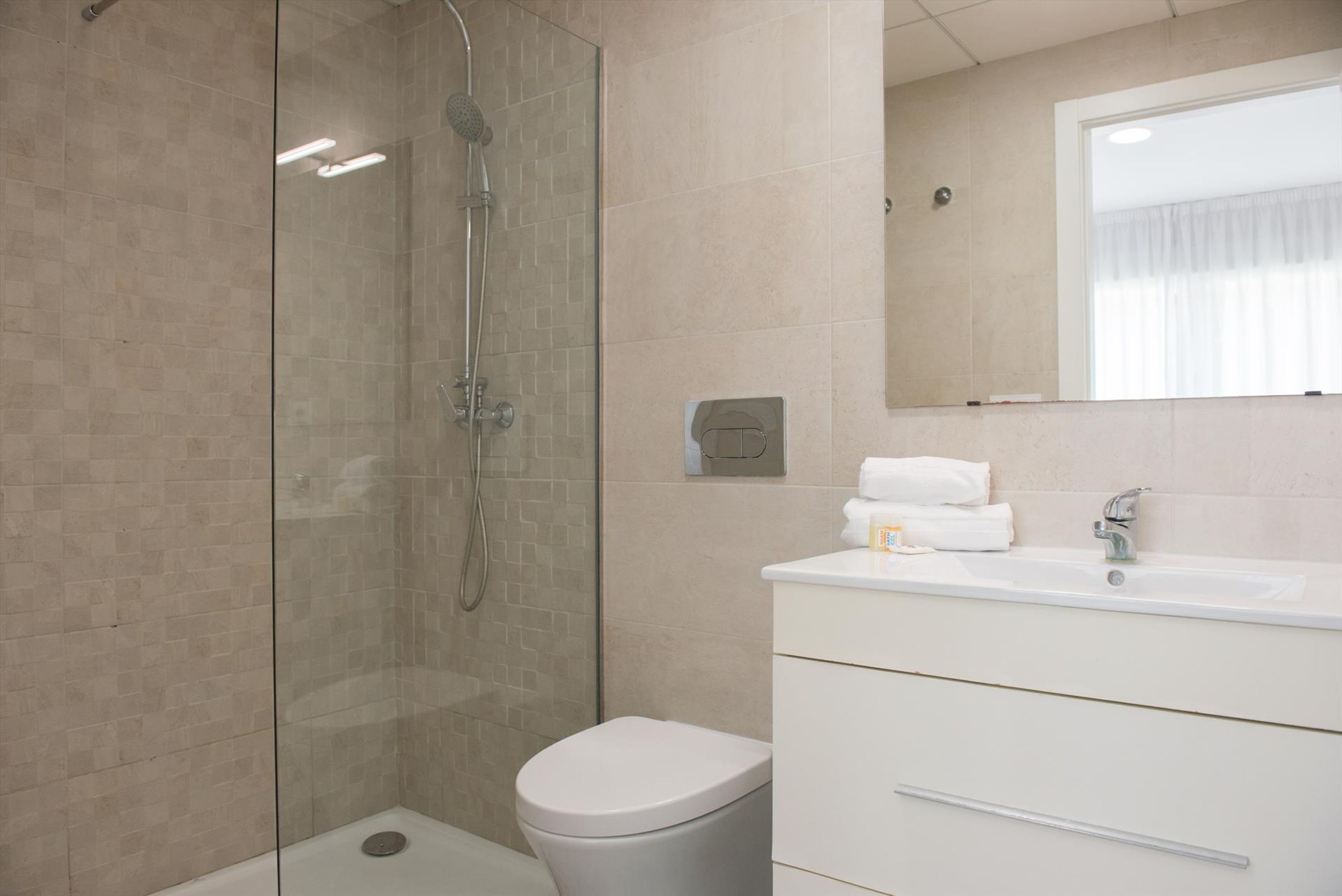 Une salle de bain moderne avec une douche à parois de verre, des toilettes blanches et un meuble-lavabo doté d’un miroir et d’un évier.