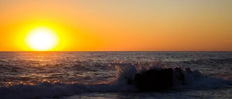 A sunset over the ocean with waves crashing onto rocks.