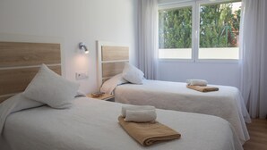 A hotel room with two beds, each with a white bedspread and pillows, a nightstand with a lamp, and a window with curtains. - Marina A3 4 pax in Balc n del Mar (Denia)
