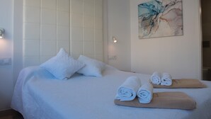 A hotel room with a bed, pillows, a towel rack, and a painting on the wall. - Marina B2 in Balc n del Mar (Denia)