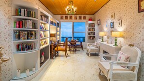 A cozy reading room with bookshelves, a fireplace, and a view of the outdoors. - The English Country House (Mussoorie)