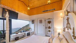 A bedroom with a large bed, a desk with a computer, and a view of the outdoors. - The English Country House (Mussoorie)