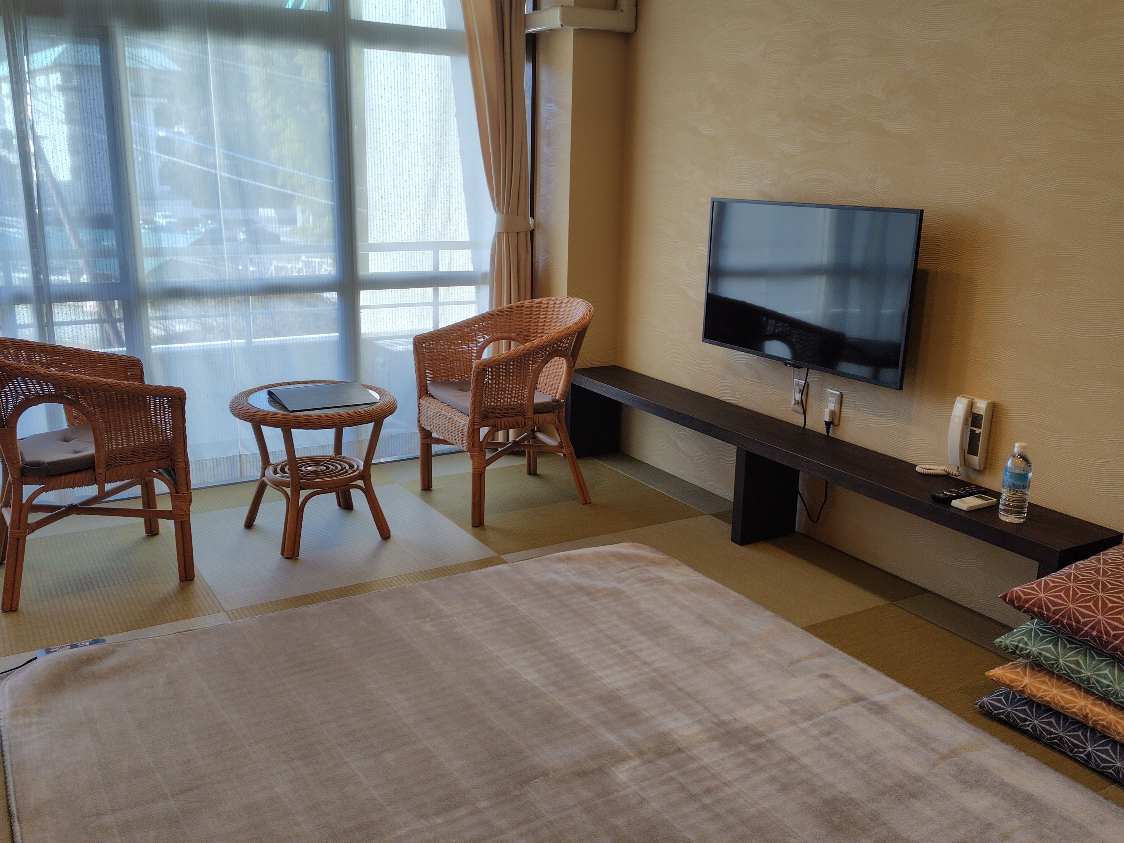 Une chambre d’hôtel équipée d’une télévision, de meubles en osier, d’une grande fenêtre et d’un téléviseur à écran plat fixé au mur.