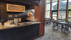 Zona de recepción de hotel con diseño moderno, que incluye un mostrador de recepción, un elemento decorativo en la pared y vistas a las montañas a través de amplios ventanales.