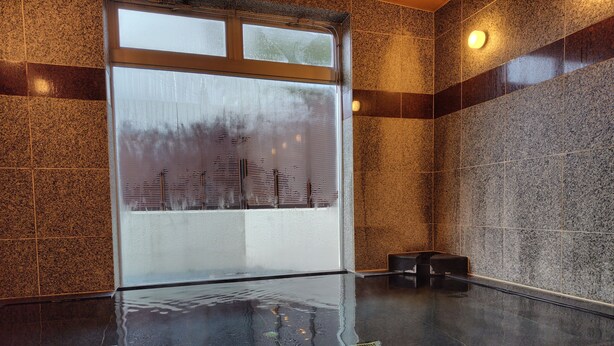 Zona de spa con ventanal de vidrio, suelo mojado y pared de azulejos.