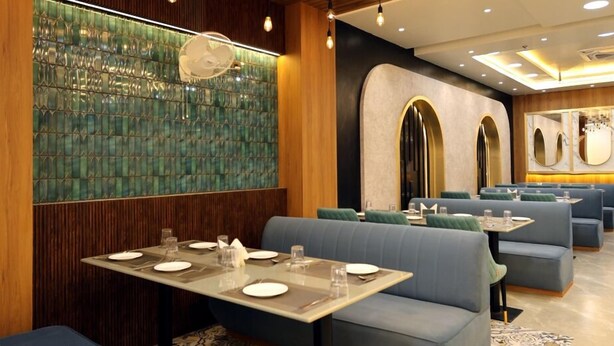A modern restaurant interior with wooden ceiling panels, hanging light fixtures, and blue upholstered booths. - Hotel RGS Crystal (Kanpur)