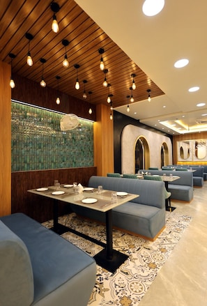 L’intérieur d’un restaurant, avec des banquettes, des tables et des luminaires suspendus.