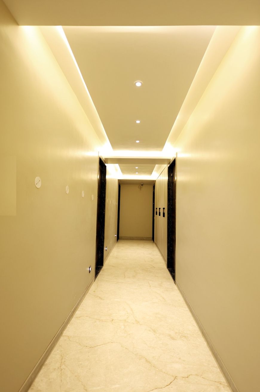 A hotel hallway with a marble floor, recessed lighting, and a door at the end.