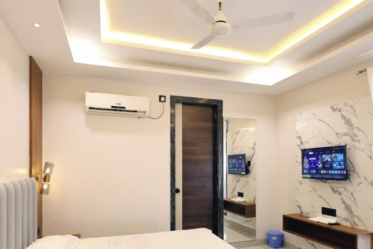 Ein modernes Hotelzimmer mit einem großen Bett, Deckenventilator, Klimaanlage, Fernseher, Marmorwand und einer kleinen Ablagefläche.