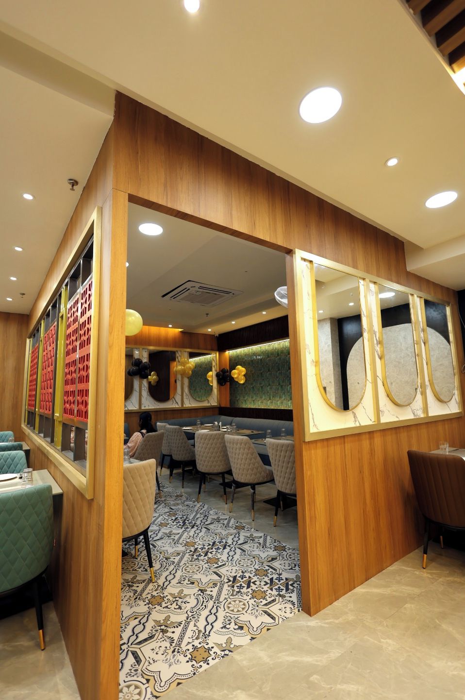 A modern restaurant with wooden paneling, patterned flooring, and a central seating area with tables and chairs.