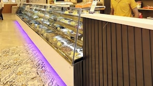 A modern interior with a reception desk, a display case of food items, and a patterned carpet. - Hotel RGS Crystal (Kanpur)